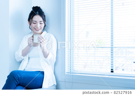 A woman relaxing with a cup of coffee in the sunny living room 82527916