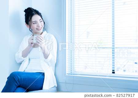 A woman relaxing with a cup of coffee in the sunny living room 82527917