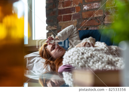 Cropped portrait of young girl lying on sofa suffering from a cold, flu. Home isolation 82533356