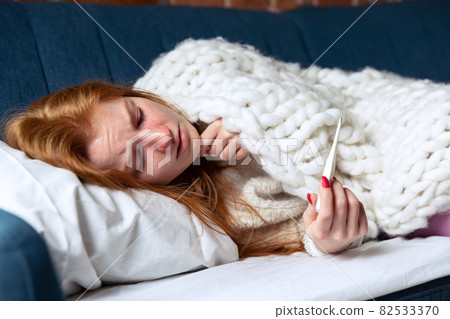 Cropped portrait of young girl lying on sofa, measuring temperature. Feeling sick. Cropped portrait of young girl lying on sofa, measuring temperature. Feeling sick. 82533370