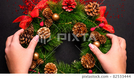 Female hands holding christmas wreath over black background with glitter and copy space Female hands holding christmas wreath over black background with glitter and copy space 82533444