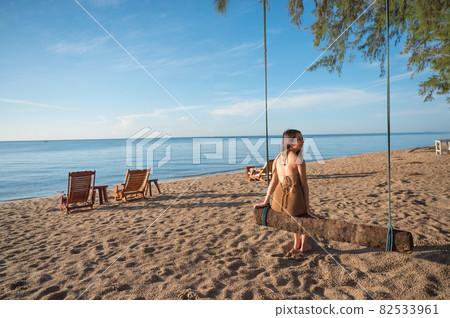Asian woman sitting at wooden swing on the beach in tropical sea at morning Asian woman sitting at wooden swing on the beach in tropical sea at morning 82533961