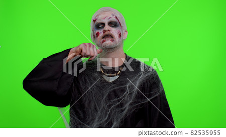 Sinister man Halloween zombie trying to scare showing killing gesture, runs a finger along his neck Sinister man Halloween zombie trying to scare showing killing gesture, runs a finger along his neck 82535955