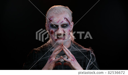 Creepy man with Halloween zombie bloody wounded makeup, trying to scare, praying, horror theme 82536672
