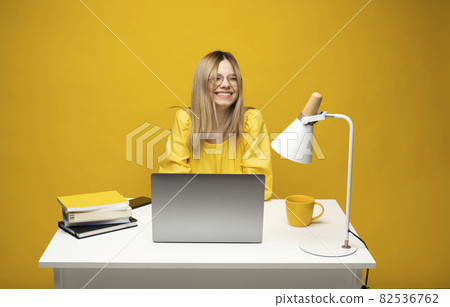 Excited young woman working with a grey laptop computer, notebook while sitting at the table with grey laptop. Smiling business woman or student received a good news isolated on a yellow background. Excited young woman working with a grey laptop computer, notebook while sitting at the table with grey laptop. Smiling business woman or student received a good news isolated on a yellow background. 82536762