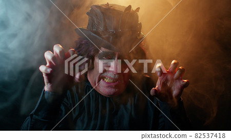 Sinister man with horrible scary Halloween witcher makeup in costume making faces trying to scare 82537418