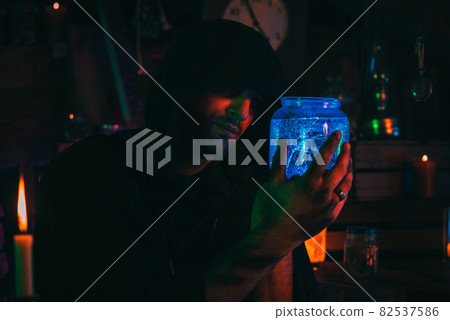 alchemist magician holds a flask with a potion in hands. Sorcerer is witcher in dark laboratory 82537586