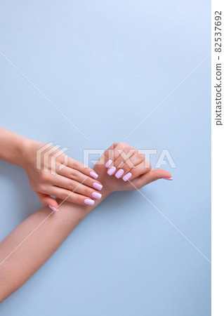 Hands of a beautiful woman on a blue background. Delicate hands with natural pink manicure, clean skin. Hands of a beautiful woman on a blue background. Delicate hands with natural pink manicure, clean skin. 82537692