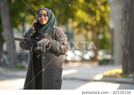 Portrait of a muslim girl in a green hijab with a scooter on the street Portrait of a muslim girl in a green hijab with a scooter on the street 82538136