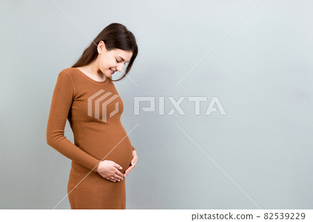 Happy pregnant woman touching her abdomen at Colored background. Future mother is wearing white underwear. Expecting of a baby. Copy space 82539229