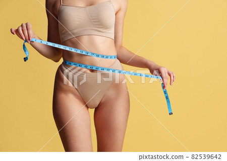 Close-up slim female body with well kept skin in pastel color panties isolated over yellow studio background. 82539642