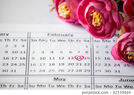 Calendar Reminder close up - Valentine's Day February 14th. Date in a red circle closeup on a background of flowers. Selective focus 82539884