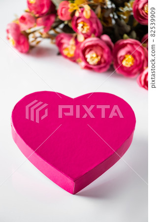 Pink heart for valentines day on a background of flowers. Close-up pink heart and a bouquet of flowers on a white background. Place for text, vertical photo. 82539909