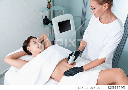 Beautiful woman having cavitation, procedure removing cellulite on legs and belly at beauty clinic Beautiful woman having cavitation, procedure removing cellulite on legs and belly at beauty clinic 82543295