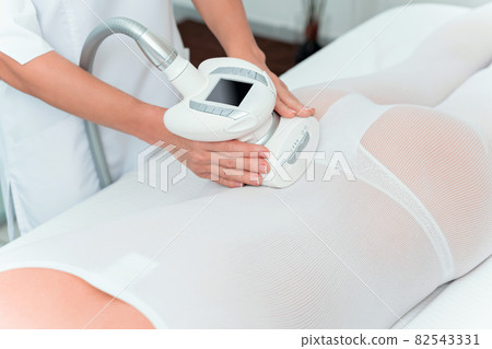 Woman in special white suit getting anti cellulite massage in a spa salon. LPG, and body contouring treatment in clinic. Woman in special white suit getting anti cellulite massage in a spa salon. LPG, and body contouring treatment in clinic. 82543331