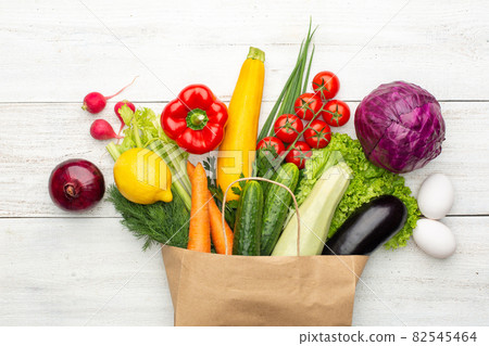 Set of vegetables and herbs in a paper bag on a white wooden background. 82545464