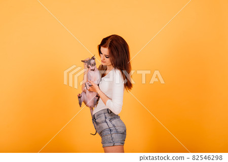 Gorgeous brunette woman smiling, holding Sphynx kitten, posing on grey and yellow studio background. Gorgeous brunette woman smiling, holding Sphynx kitten, posing on grey and yellow studio background. 82546298