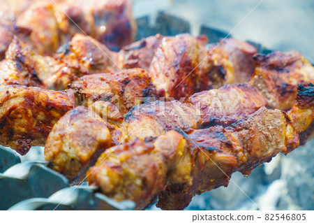 Appetizing raw meat kebab is cooked on the grill on the wood, in the open air. The kebab is cooked on skewers. 82546805