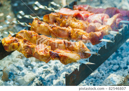 Appetizing raw meat kebab is cooked on the grill on the wood, in the open air. The kebab is cooked on skewers. Appetizing raw meat kebab is cooked on the grill on the wood, in the open air. The kebab is cooked on skewers. 82546807