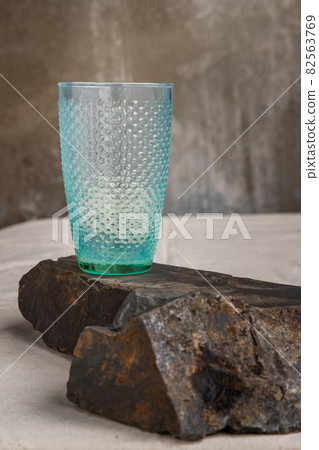 A blue glass cup for water drinking and surface reflections on rock floor. A blue glass cup for water drinking and surface reflections on rock floor. 82563769