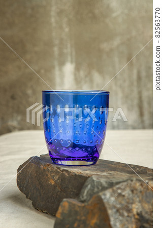 A blue glass cup for water drinking and surface reflections on rock floor. A blue glass cup for water drinking and surface reflections on rock floor. 82563770