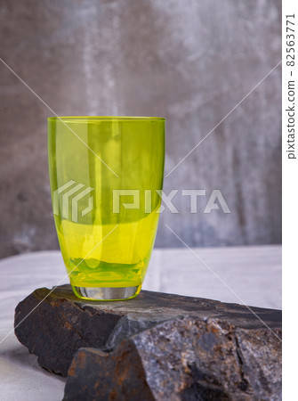 A green glass cup for water drinking and surface reflections on rock floor. A green glass cup for water drinking and surface reflections on rock floor. 82563771