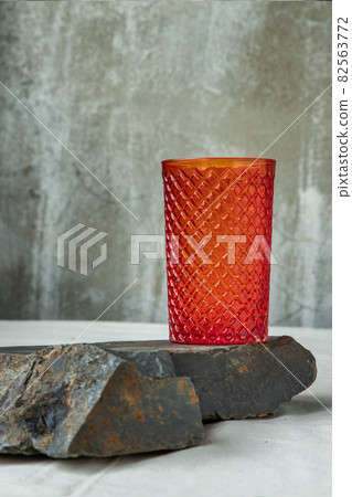 A red glass cup for water drinking and surface reflections on rock floor. A red glass cup for water drinking and surface reflections on rock floor. 82563772