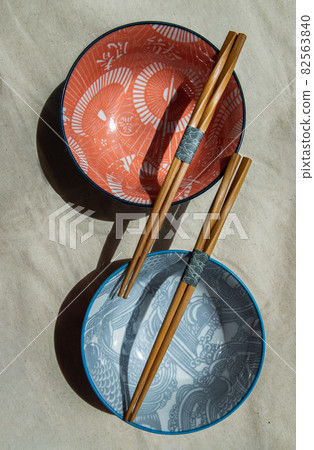 Two ceramics bowls with wooden chopsticks  on calico fabric cloth. 82563840