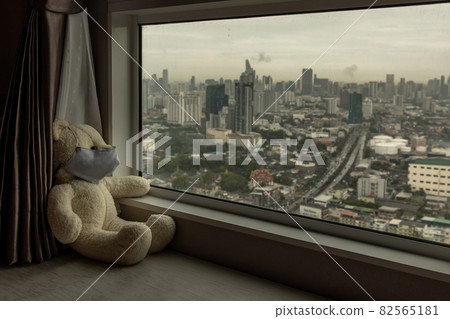 Sad teddy bear in protective medical masks sits on windowsill and looks out window. Sad teddy bear in protective medical masks sits on windowsill and looks out window. 82565181