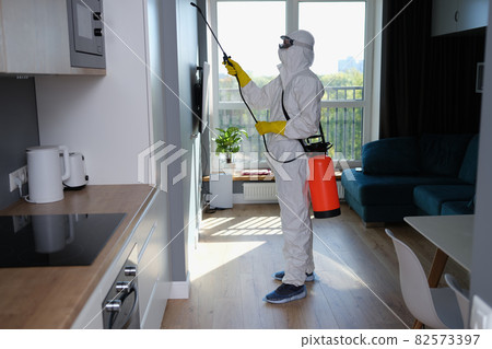 Person in white protective suit, mask and gloves with balloon disinfection in kitchen Person in white protective suit, mask and gloves with balloon disinfection in kitchen 82573397