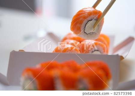 Hand with disposable chopsticks holds sake nigiri sushi with salmon fish 82573398