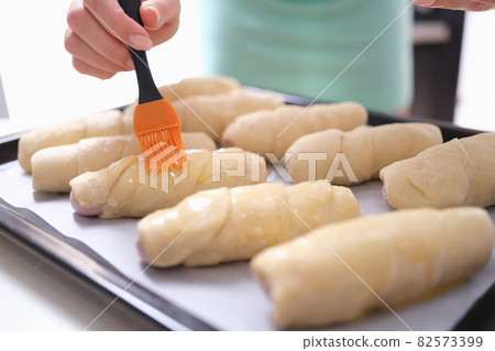 Woman hand is brushing egg yolk onto sweet flour rolls Woman hand is brushing egg yolk onto sweet flour rolls 82573399