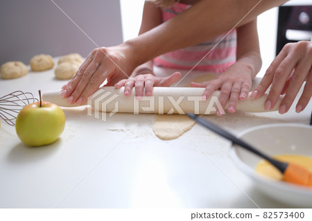 Mom and daughter roll out dough with rolling pin in kitchen Mom and daughter roll out dough with rolling pin in kitchen 82573400