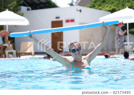 Young woman in sunglasses is engaged in aqua aerobics in outdoor pool Young woman in sunglasses is engaged in aqua aerobics in outdoor pool 82573495