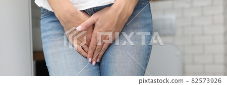 Woman stands in bathroom and covers her lower abdomen with her hand Woman stands in bathroom and covers her lower abdomen with her hand 82573926