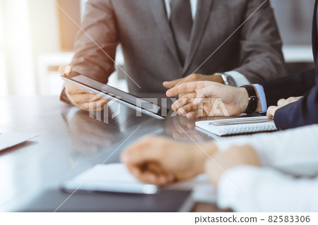 Unknown businessman using tablet computer and working together with his colleague while sits at the glass desk in modern office. Teamwork and partnership concept 82583306
