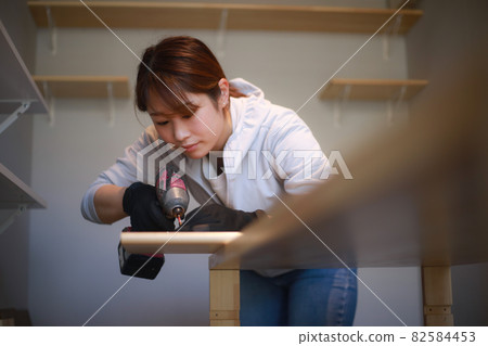 Woman tightening screws with an electric screwdriver 82584453