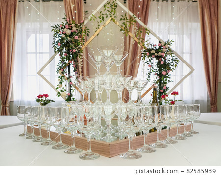Empty wine glasses on a table are a pyramid. Beautiful wedding ceremony indoors. 82585939