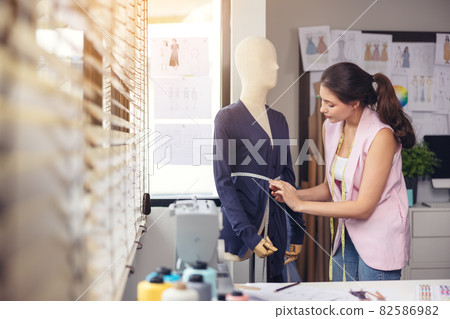 Portrait of a young, attractive woman on a stylish fashion designer's table, surrounded by color textile samples. Attractive woman working in a fashion studio with mannequins and colorful cloths. Portrait of a young, attractive woman on a stylish fashion designer's table, surrounded by color textile samples. Attractive woman working in a fashion studio with mannequins and colorful cloths. 82586982