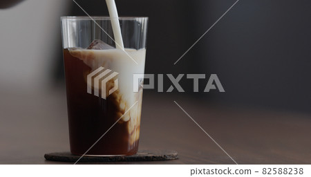 pour milk into ice coffee on black walnut table pour milk into ice coffee on black walnut table 82588238