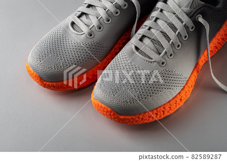 Gray textile sneakers with orange sole over grey background. Gray textile sneakers with orange sole over grey background. 82589287