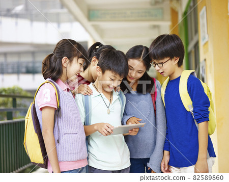 group of asian pupils looking at tablet computer in the hallway at school 82589860