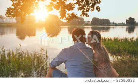 A young couple sits on a lake at sunset. 82590058