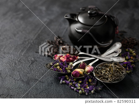 Teapot with spoons with various tea on black background. Rose buds,blue mallow flowers 82590311
