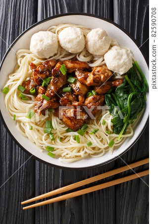 Mie ayam, mi ayam or bakmi ayam is a common Indonesian dish of seasoned noodles topped with diced chicken meat and meatball closeup in the bowl. Vertical top view 82590708