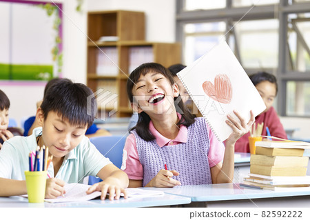 happy and lovely asian elementary school girl showing a drawing and laughing happy and lovely asian elementary school girl showing a drawing and laughing 82592222
