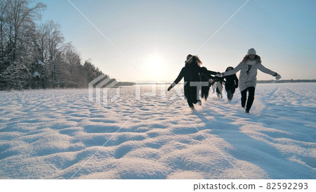 Cheerful girls run hand in hand across a snowy field. 82592293