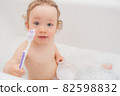 Funny happy baby with curly hair taking bath and brushing her teeth. A cute baby girl is happy in the bathroom 82598832