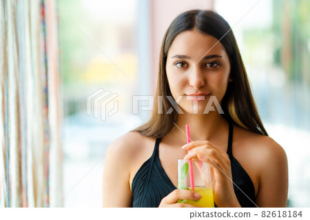 Young woman smiling and drinking some beverage in front of window. Young woman smiling and drinking some beverage in front of window. 82618184