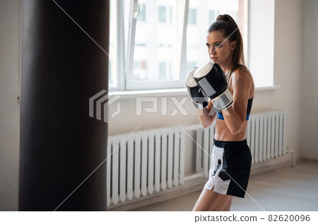 Beautiful kickboxing woman training punching bag in fitness studio. Beautiful kickboxing woman training punching bag in fitness studio. 82620096